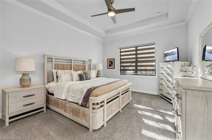 Bedroom featuring a raised ceiling, light colored carpet, a ceiling fan, and ornamental molding