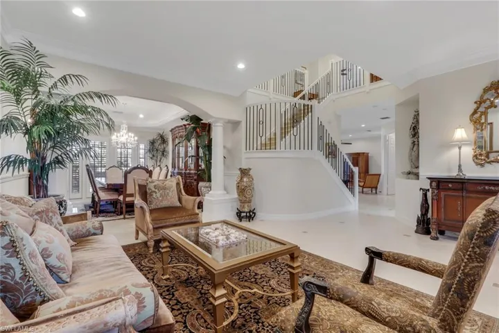 Living area featuring ornamental molding, arched walkways, a chandelier, ornate columns, and recessed lighting