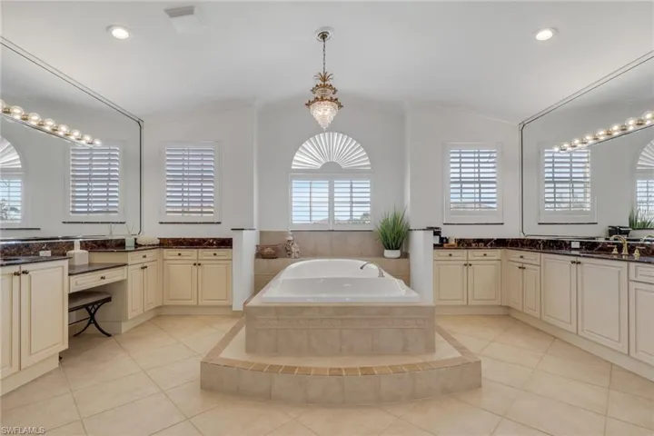 Bathroom with two vanities, a garden tub, light tile patterned flooring, recessed lighting, and vaulted ceiling