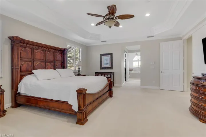 Bedroom with light colored carpet, ornamental molding, a raised ceiling, ceiling fan, and connected bathroom