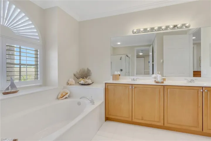 Full bathroom featuring a garden tub, double vanity, crown molding, and a stall shower