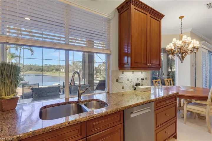 Kitchen with brown cabinetry, stainless steel dishwasher, ornamental molding, light stone countertops, and a chandelier