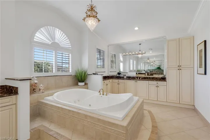 Full bathroom with vanity, a chandelier, a tub with jets, crown molding, and light tile patterned flooring