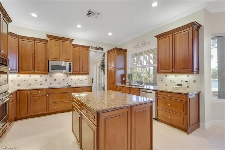 Kitchen with backsplash, brown cabinetry, light stone countertops, stainless steel appliances, and ornamental molding