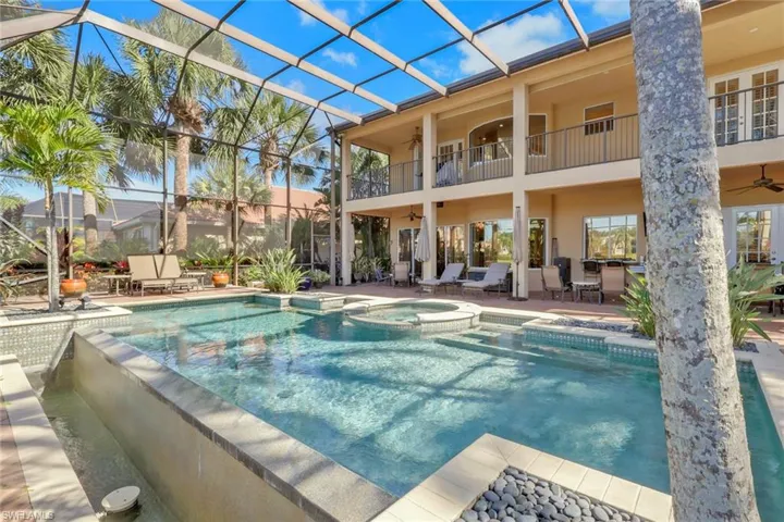 View of pool featuring a patio area, glass enclosure, a pool with connected hot tub, and a balcony