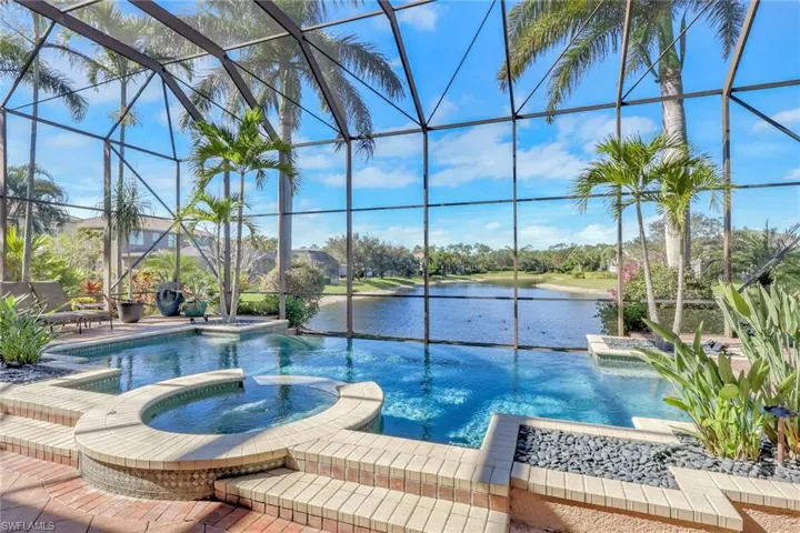 View of pool featuring a pool with connected hot tub, glass enclosure, a water view, a sunroom, and a patio area