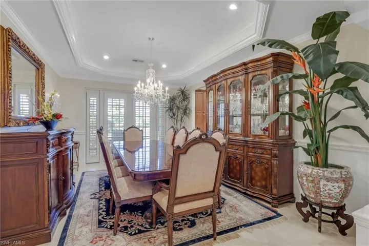 Dining space with crown molding, a raised ceiling, a chandelier, recessed lighting, and light tile patterned floors