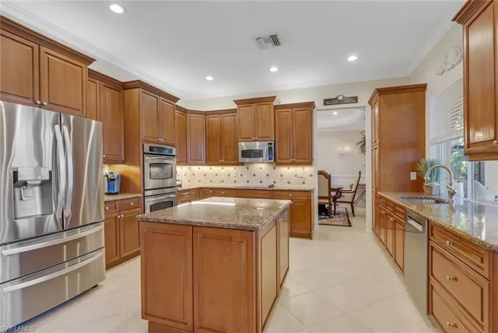 Kitchen featuring appliances with stainless steel finishes, brown cabinetry, light stone countertops, ornamental molding, and backsplash