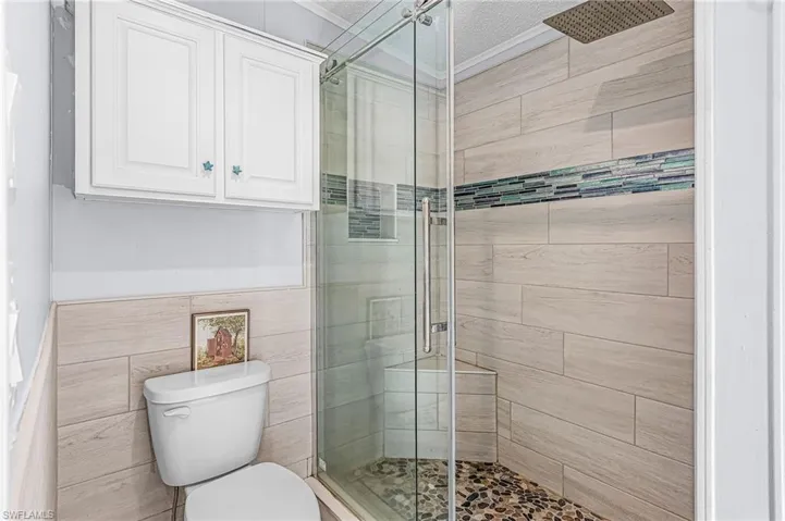 Bathroom featuring a stall shower, tile walls, wainscoting, and a textured ceiling