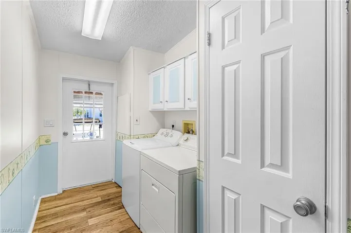 Laundry room featuring a textured ceiling, light wood-type flooring, cabinet space, and separate washer and dryer