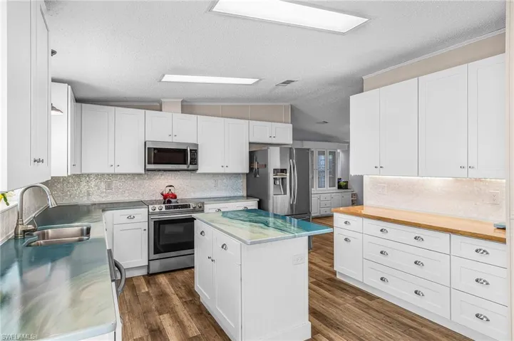 Kitchen with stainless steel appliances, stainless steel counters, white cabinetry, tasteful backsplash, and a center island