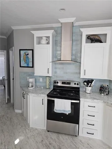 Kitchen with wall chimney range hood, crown molding, tasteful backsplash, and electric stove