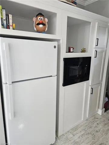 Kitchen with freestanding refrigerator, black microwave, white cabinetry, and light wood-style floors
