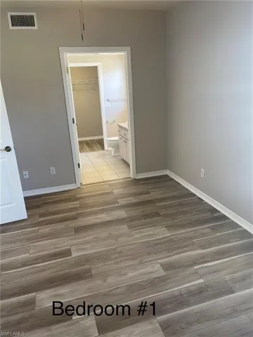 Unfurnished bedroom featuring light wood-style laminate flooring, a spacious closet, and ensuite bath