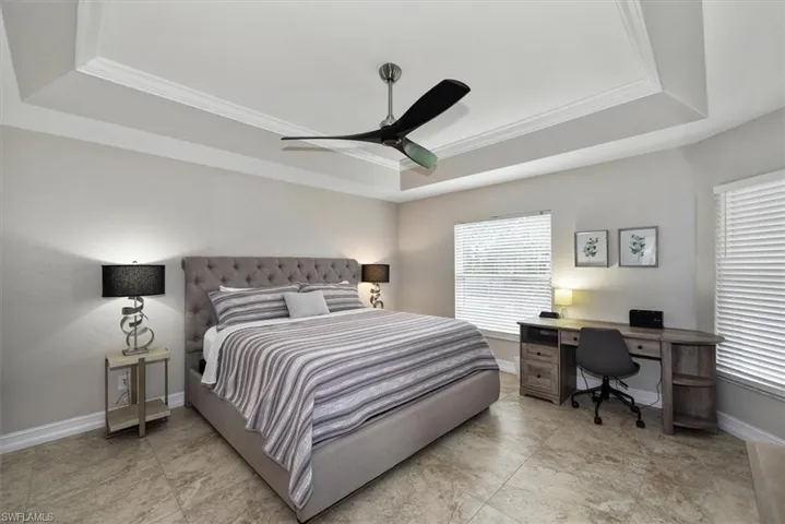 Bedroom featuring a tray ceiling, ornamental molding, ceiling fan, and an office area