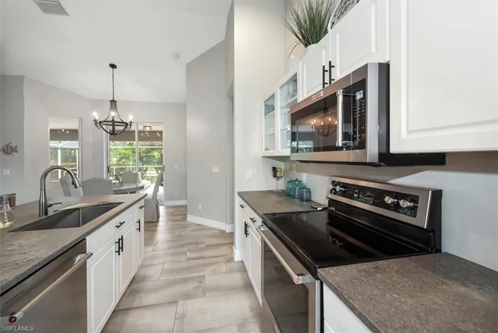 Kitchen with stainless steel appliances, dark countertops, a chandelier, white cabinetry, and glass insert cabinets