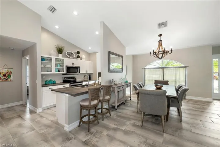 Kitchen with appliances with stainless steel finishes, dark countertops, a chandelier, white cabinets, and a kitchen bar