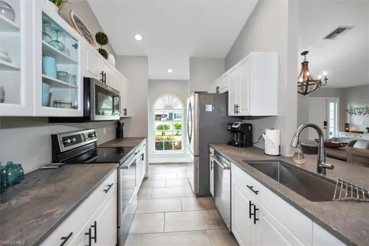Kitchen with stainless steel appliances, white cabinets, glass insert cabinets, a chandelier, and light tile patterned flooring