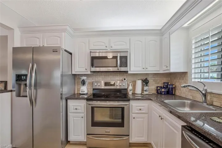 Kitchen featuring a sunny window,white cabinetry, stainless steel appliances, dark countertops, a tiled backsplash, and a stainless steel sink