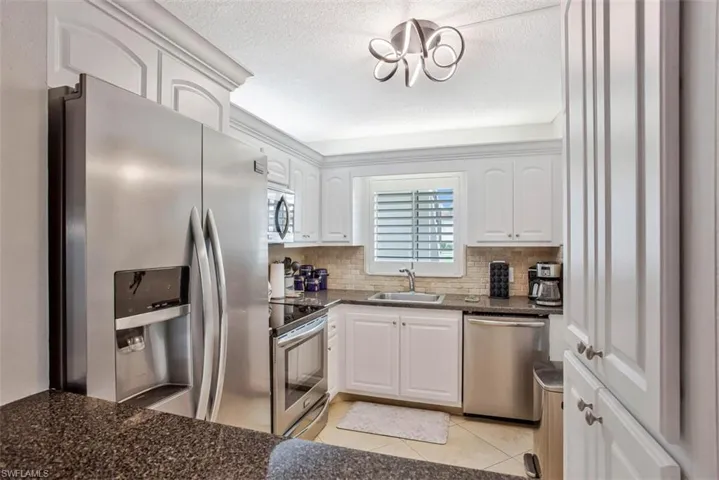 Modern kitchen with white cabinetry, stainless steel appliances, dark stone countertops, and a tiled backsplash