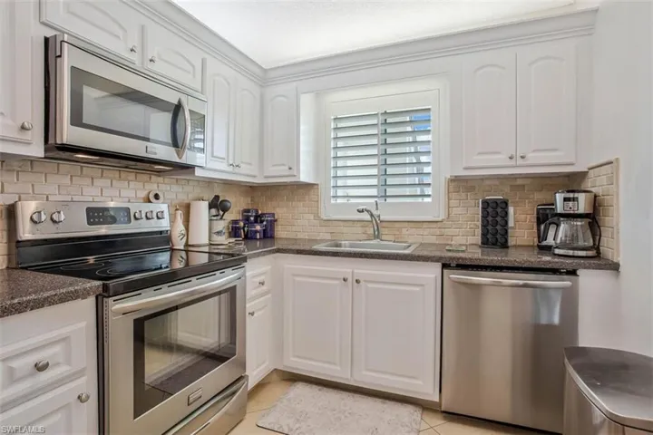 White cabinetry, stainless steel appliances, stone-finish countertops, tiled backsplash