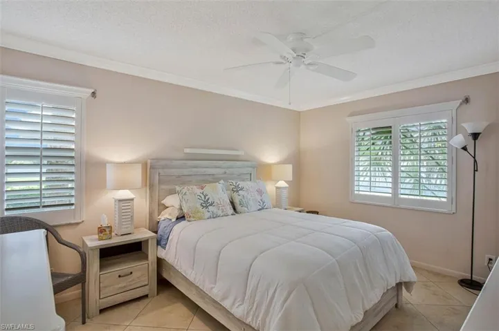 Crown molding with an overhead ceiling fan, dual windows featuring plantation shutters, and light-toned tile flooring