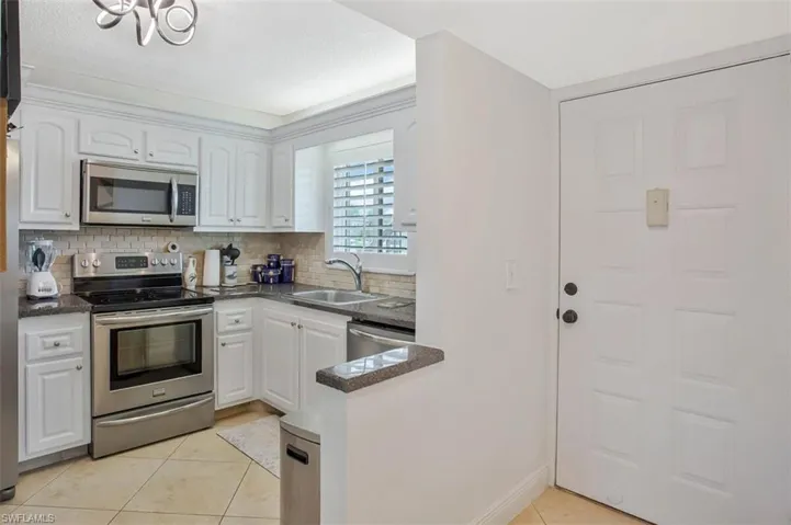 Updated Kitchen featuring white cabinetry, stainless steel appliances,  stone countertops, a tiled backsplash, and tiled flooring