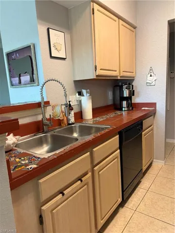 Kitchen with a textured wall, light wood finish cabinets, dishwasher, and light tile patterned floors