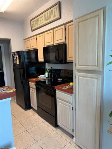 Kitchen featuring black range, a textured wall, a textured ceiling, light tile patterned flooring, and dark countertops