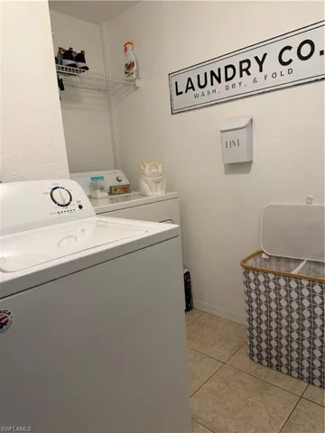 Laundry room with light tile patterned floors, washer and clothes dryer, and a textured wall