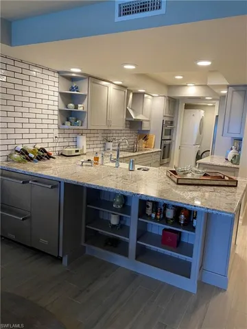 Kitchen featuring light stone countertops, dark hardwood / wood-style flooring, kitchen peninsula, wall chimney range hood, and double oven