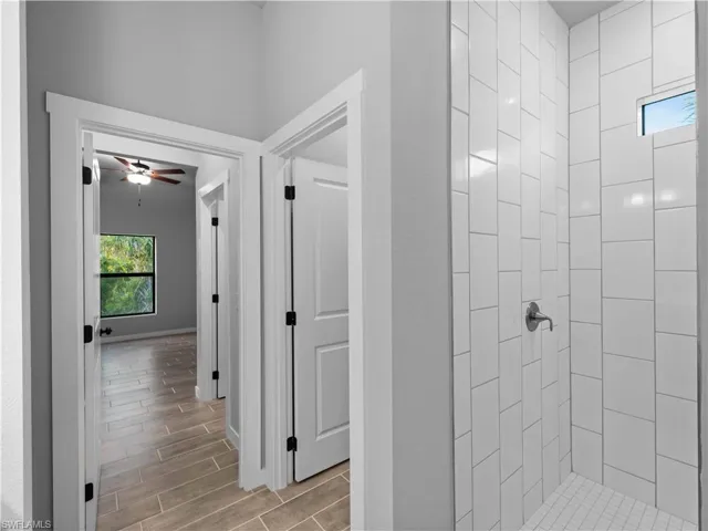 Bathroom featuring wood finish floors, a ceiling fan, tiled shower, and baseboards