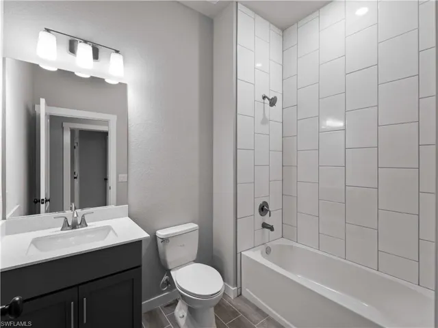 Bathroom with toilet, vanity, washtub / shower combination, baseboards, and a textured wall