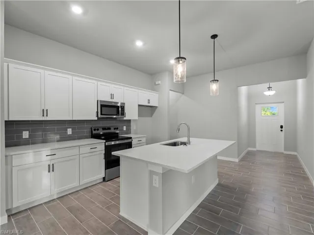 Kitchen with appliances with stainless steel finishes, a sink, tasteful backsplash, wood tiled floors, and baseboards
