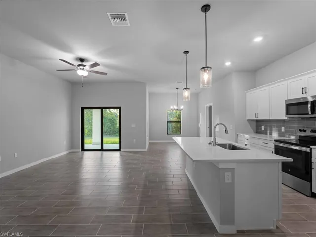 Kitchen featuring appliances with stainless steel finishes, a sink, open floor plan, a kitchen island with sink, and a ceiling fan