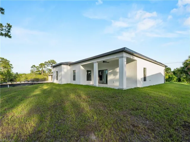 Rear view of house with stucco siding, a lawn, and a ceiling fan