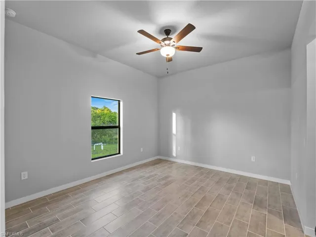 Unfurnished room featuring a ceiling fan, wood finished floors, baseboards, and a smoke detector