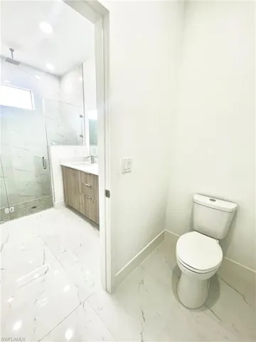Full bathroom featuring vanity, marble finish floor, toilet, baseboards, and a marble finish shower