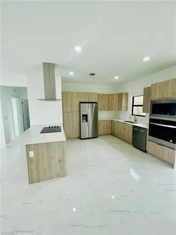 Kitchen with appliances with stainless steel finishes, ventilation hood, and modern cabinets