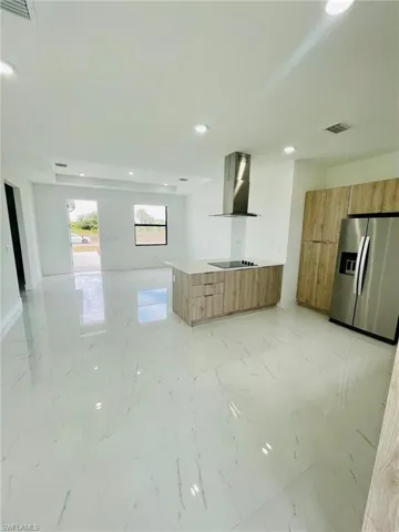 Kitchen featuring stainless steel refrigerator with ice dispenser, modern cabinets, wall chimney exhaust hood, and black electric cooktop