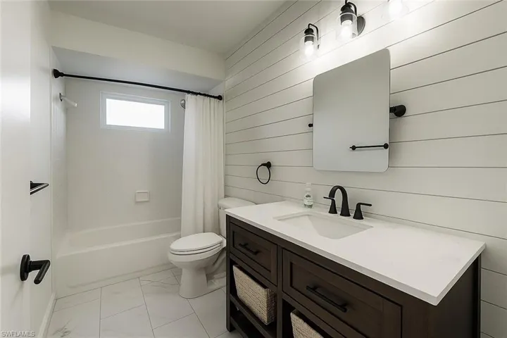 Bathroom with shower / bathtub combination with curtain, vanity, and light marble finish floors
