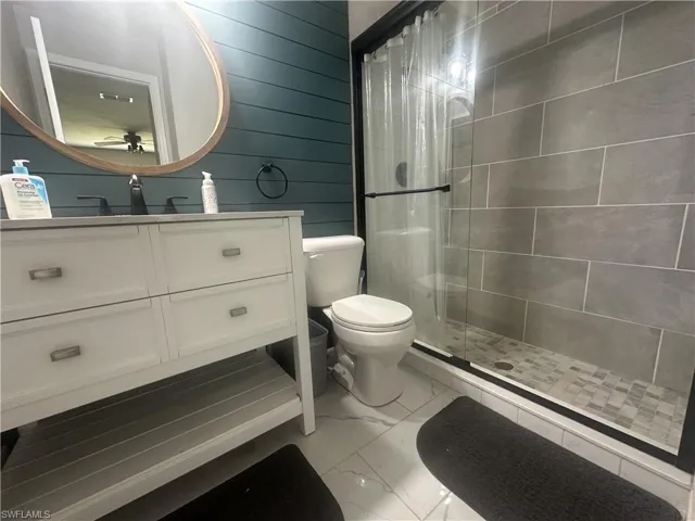 Bathroom with vanity, a stall shower, light marble finish flooring, and wood walls