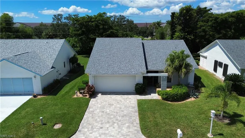 View of front of house with decorative driveway, a front yard, an attached garage, stucco siding, and a shingled roof