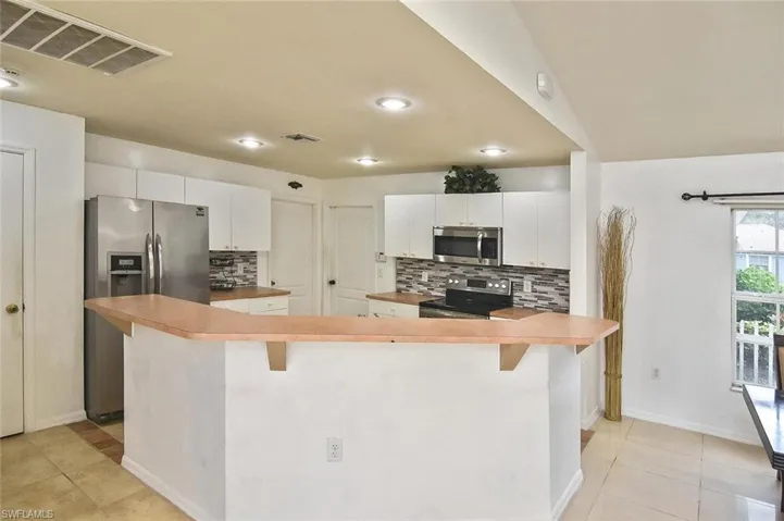 Kitchen with stainless steel appliances, white cabinets, tasteful backsplash, and light tile floors
