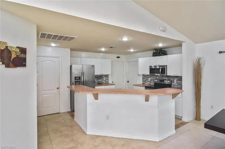 Kitchen featuring white cabinets, backsplash, a breakfast bar area, appliances with stainless steel finishes, and light tile floors