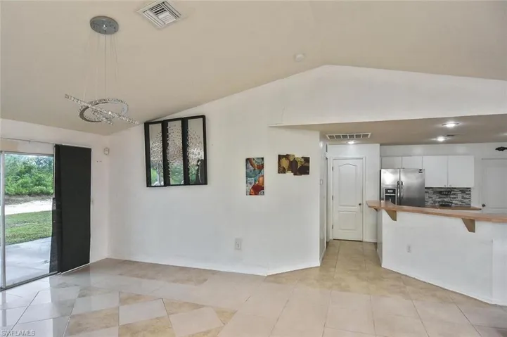 Kitchen featuring vaulted ceiling, backsplash, light tile floors, white cabinets, and stainless steel fridge with ice dispenser