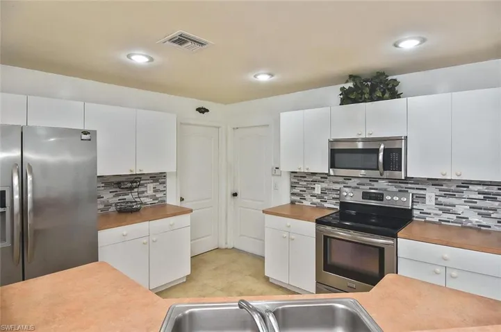 Kitchen featuring backsplash, light tile flooring, white cabinetry, and appliances with stainless steel finishes