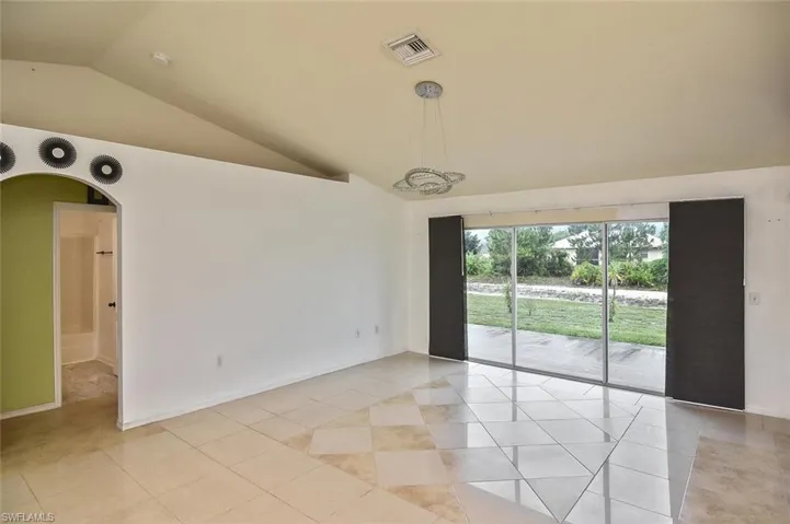 Tiled empty room featuring vaulted ceiling