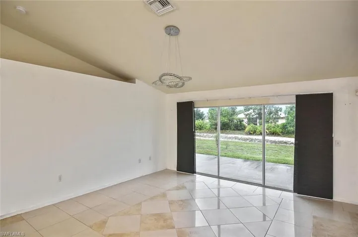 Tiled empty room featuring vaulted ceiling