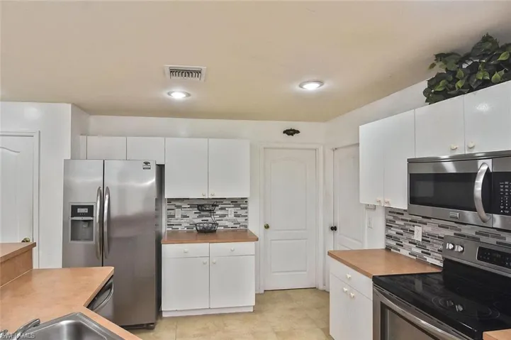 Kitchen featuring white cabinets, wood counters, backsplash, appliances with stainless steel finishes, and light tile floors